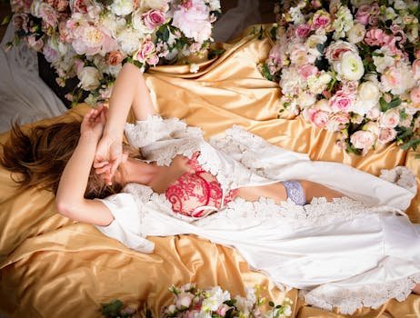 Top 5 Tendințe Incitante în Lenjeria Intimă și Îmbrăcămintea Feminină în 2026 5 Elegant woman in lace lingerie lying on satin with floral arrangement.