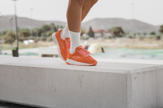 Bright orange sneakers on a concrete bench in a sunny outdoor setting.