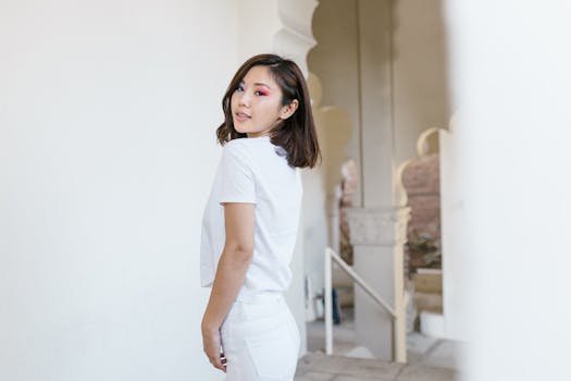 Fashionable woman with vibrant eye makeup posing indoors, wearing a white outfit.