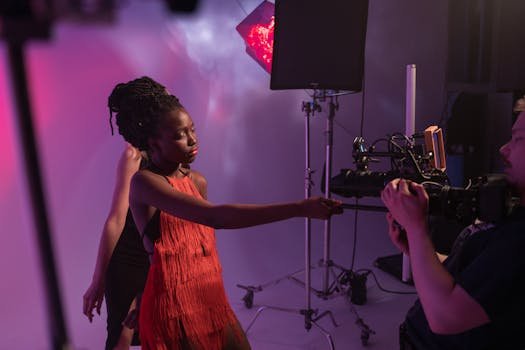 Studio photo shoot featuring model in red dress posing with camera crew under dramatic lighting.