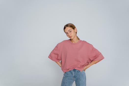 Ghidul Esențial: Cum să Alegi Lenjeria Intimă Perfectă și Îmbrăcămintea Feminină Potrivită pentru Fiecare Siluetă 4 Portrait of a woman in a pink top and denim jeans posing with hands on waist.