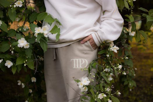 Person wearing stylish sweats with floral branches in a serene garden.