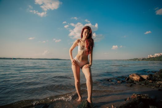 A woman stands by the water's edge in swimwear on a sunny day.
