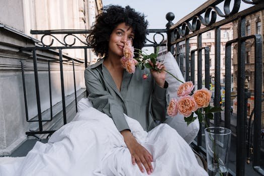 African American woman enjoys morning with roses on a city balcony, wrapped in a cozy blanket.
