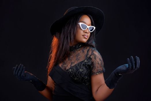 Cum să Alegi Corsetul Modelator pentru Ocazii Speciale Potrivit Siluetei Tale 2 Elegant woman in black attire, hat, gloves, and sunglasses posing against a dark background.