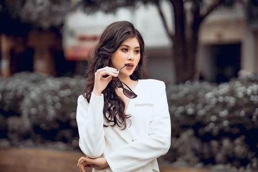 Cum să Alegi Corsetul Modelator pentru Ocazii Speciale Potrivit Siluetei Tale 4 Stylish woman with curly hair poses confidently in white clothing, holding sunglasses.