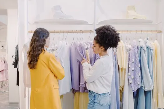 Two women selecting clothes in a chic boutique, discussing fashion choices.