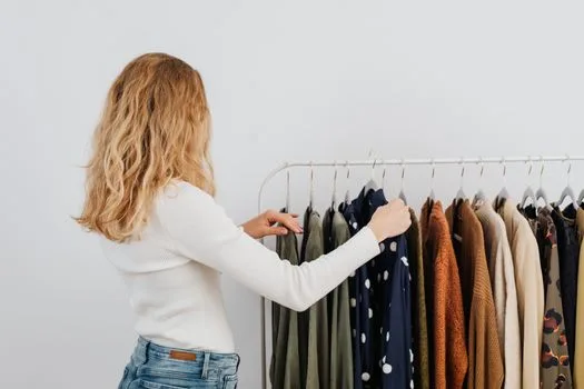 A woman browsing clothing rack in a modern boutique, wearing a white sweater.